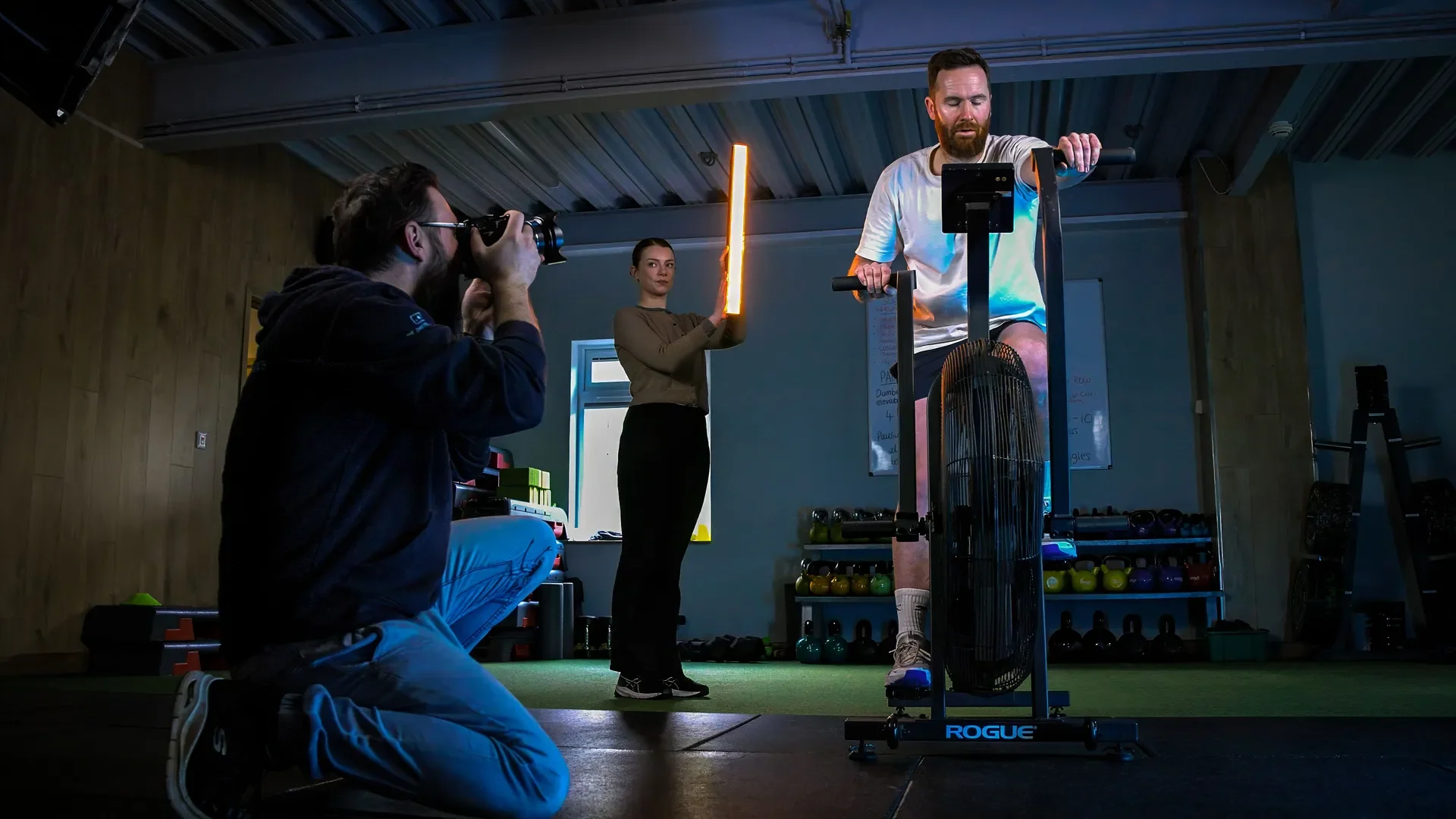 Nico van Loggerenberg photographing a man on an air bike in a gym, with a light held to one side