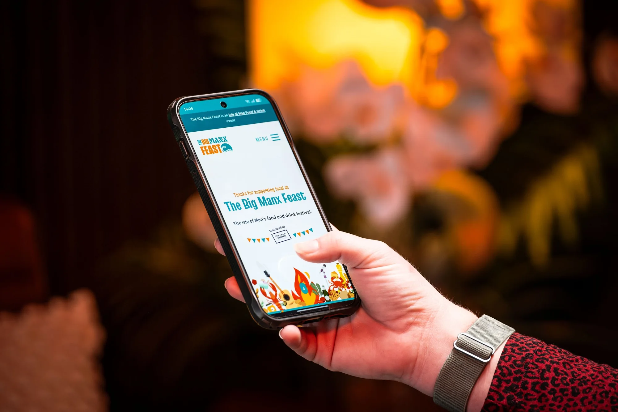The Big Manx Feast website on a phone, with the logo and the food illustrations