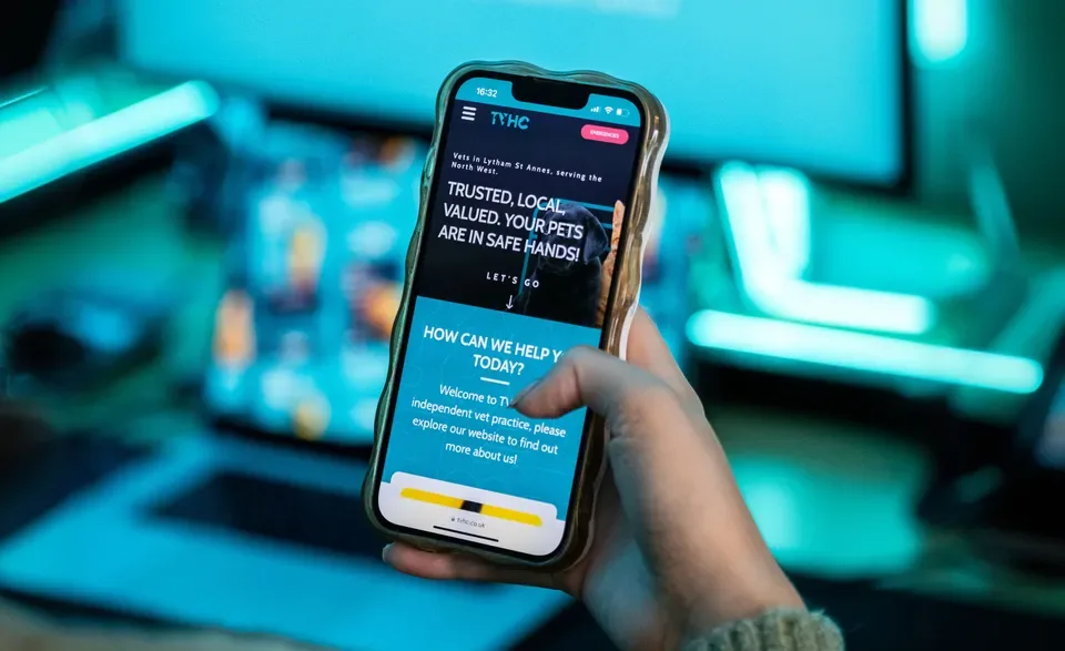 A hand holding a phone showing the TVHC veterinary practice website