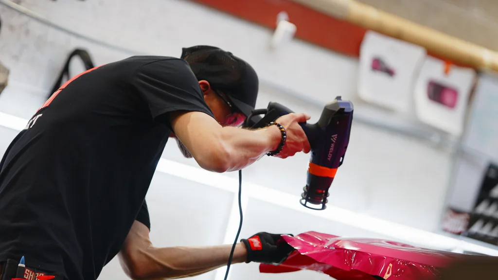 A fitter working the pink wrap into the bonnet of a Mini with a heat gun