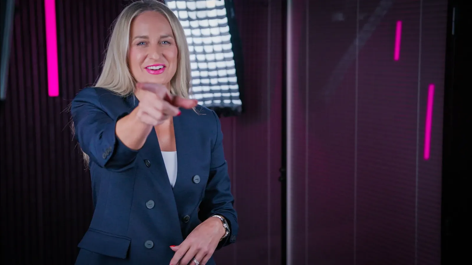 A woman in a navy blazer points forward, smiling.