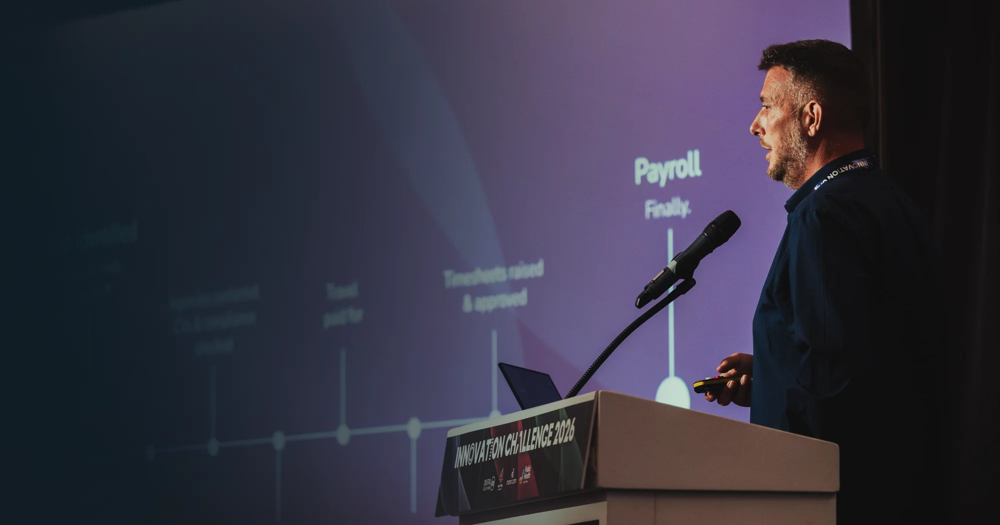 Andy Orton at the lectern at Innovation Challenge 2026, with the Payroll, finally slide behind him