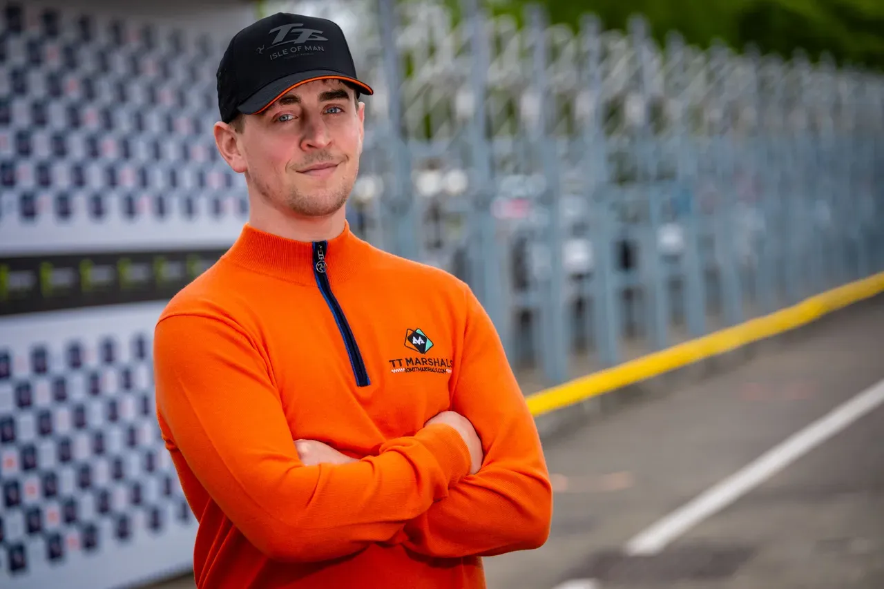 Dom Herbertson with his arms crossed in the TT Grandstand pit lane, wearing the TT Marshals prize jumper