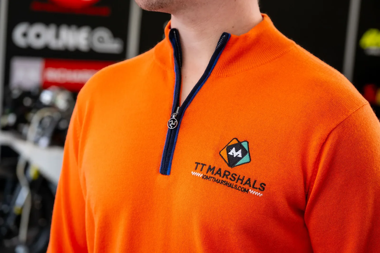 Close-up of the TT Marshals Albion Knitting Co prize jumper, showing the embroidered crest and the Manx triskelion zip pull